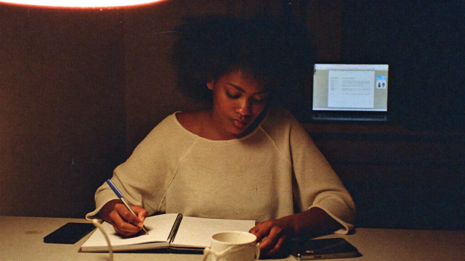 A creator at her kitchen table at night working out her numbers in a notebook