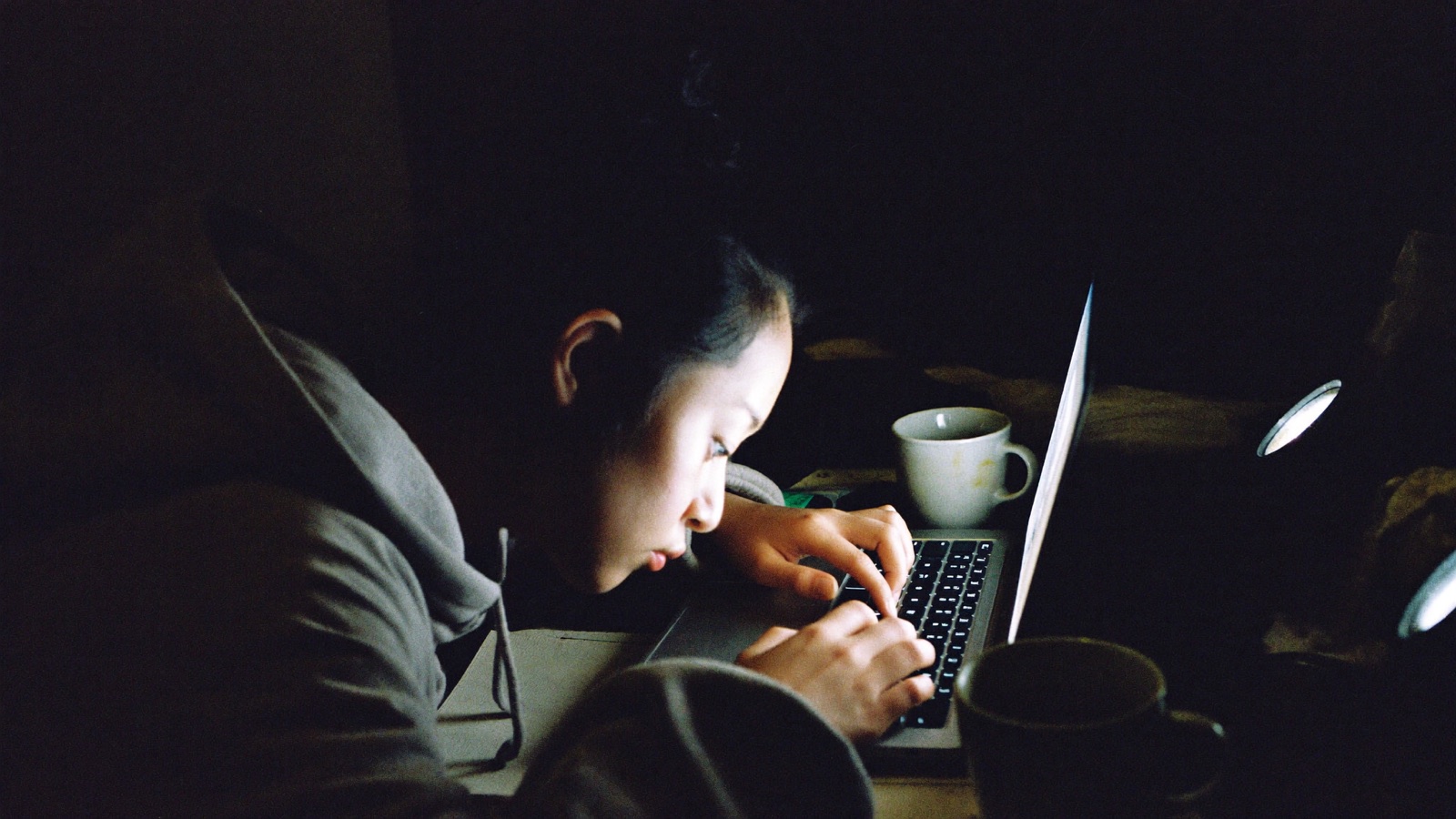 A creator answering messages late at night at a cluttered desk, lit by her laptop and a small lamp