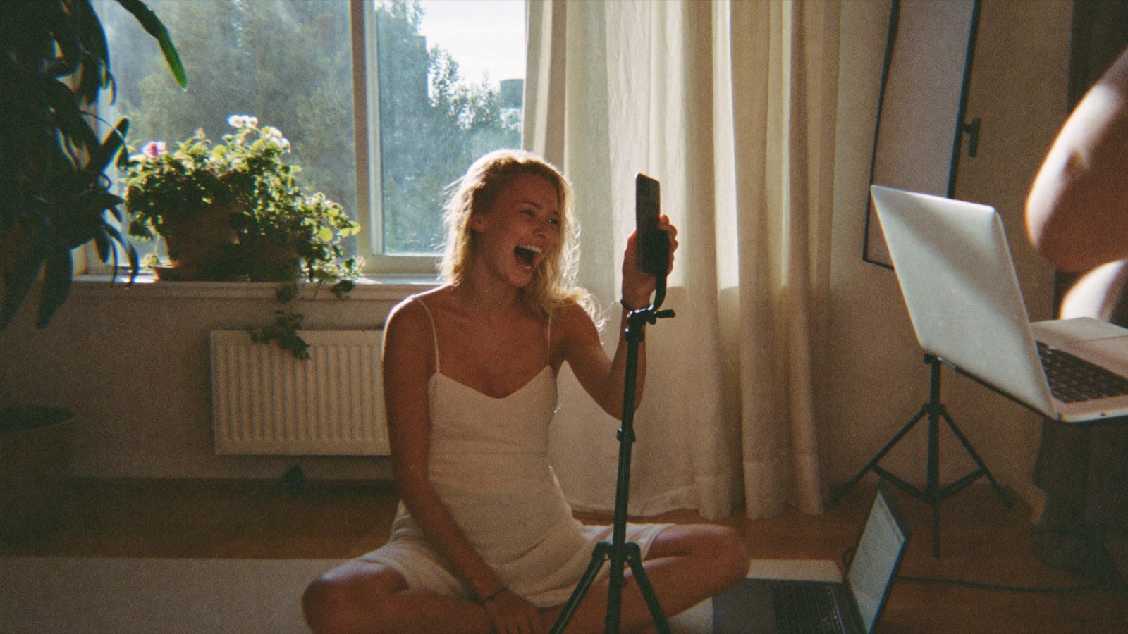 A relaxed creator filming in daylight in her living room, ring light and laptop set up by someone else