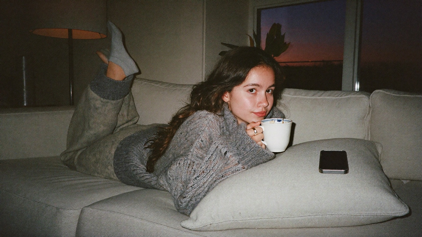 A creator relaxing on her sofa at dusk, phone face down