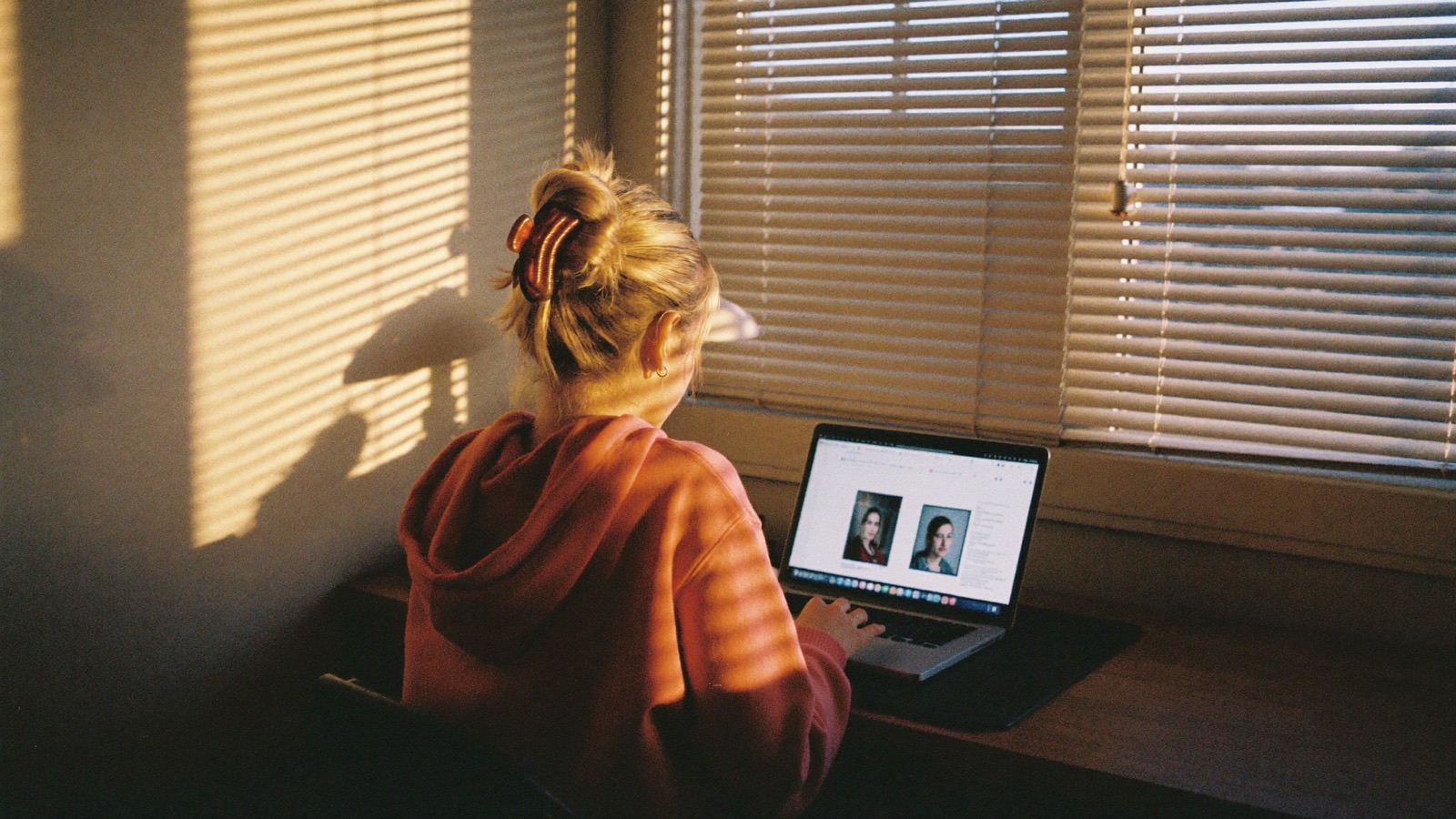 A creator at her desk behind half-closed blinds in evening light